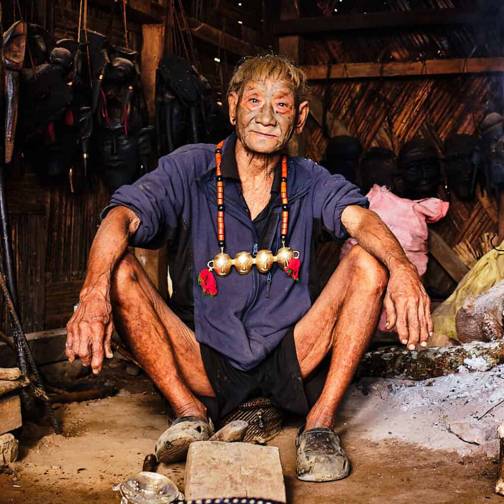 A Konyak elder with traditional facial tattoos and brass trophy necklaces. His facial tattoo and the ornaments highlights the textures of his heritage