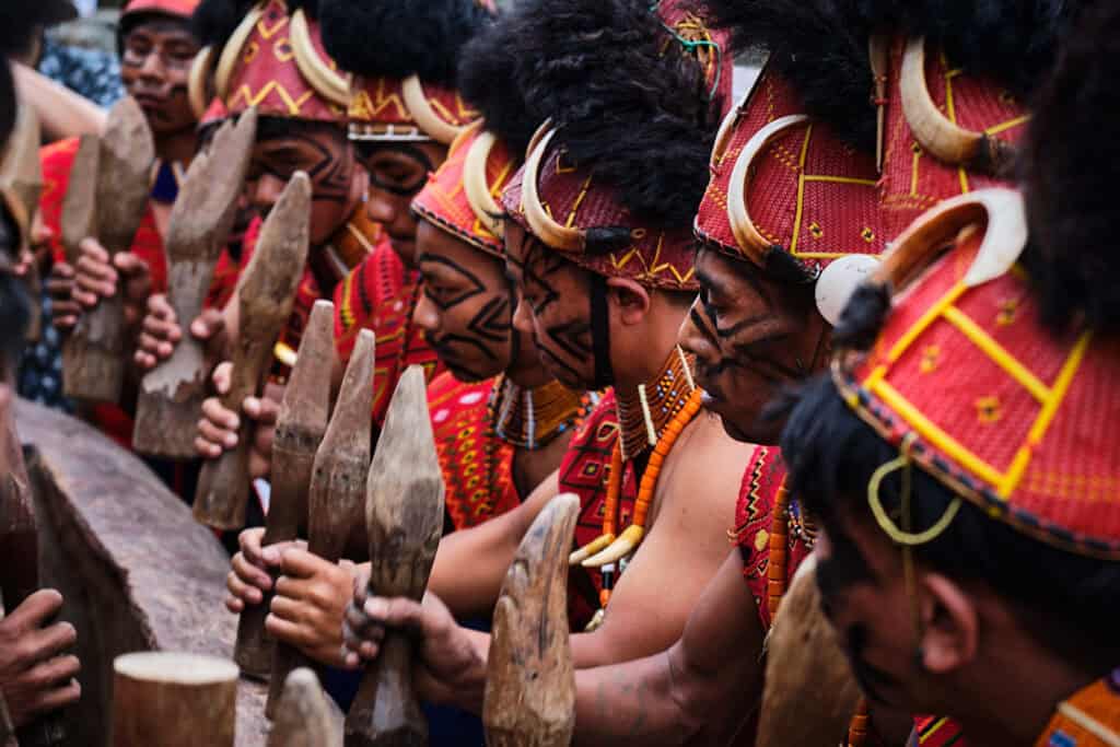 Konyak men striking a traditional log drum during the Aoling Festival, creating rhythmic beats as part of the celebration.