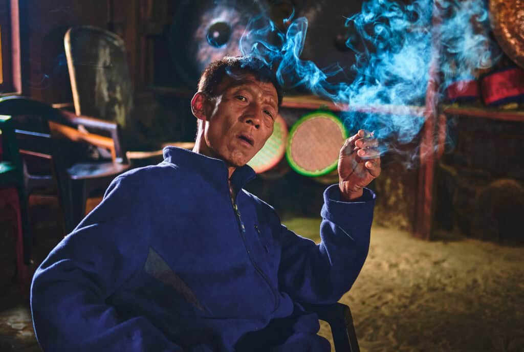 A Konyak man sitting in a dimly lit room, calmly enjoying a traditional smoke in a quiet, intimate setting.