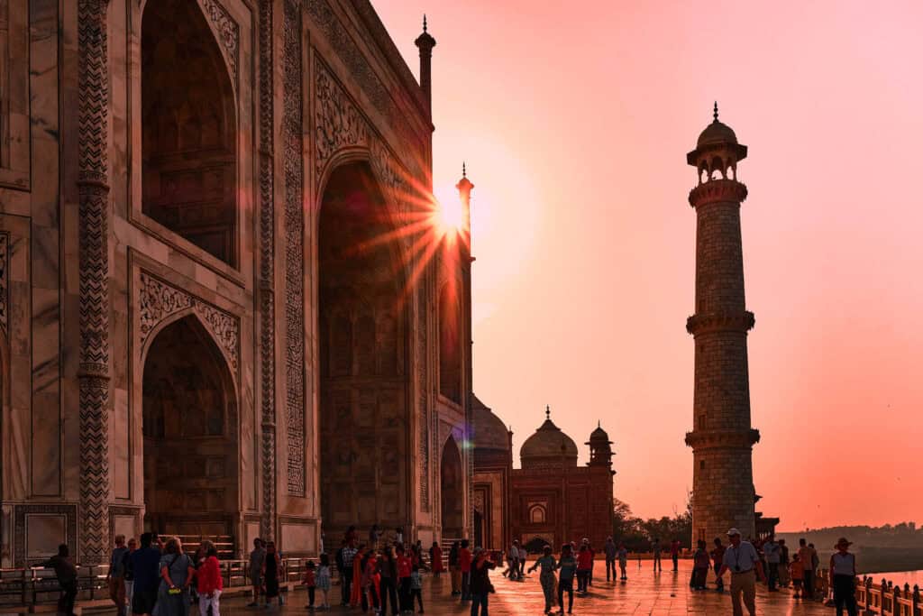 Taj Mahal glowing at sunset with a sun star effect, its white marble illuminated against the warm evening sky.