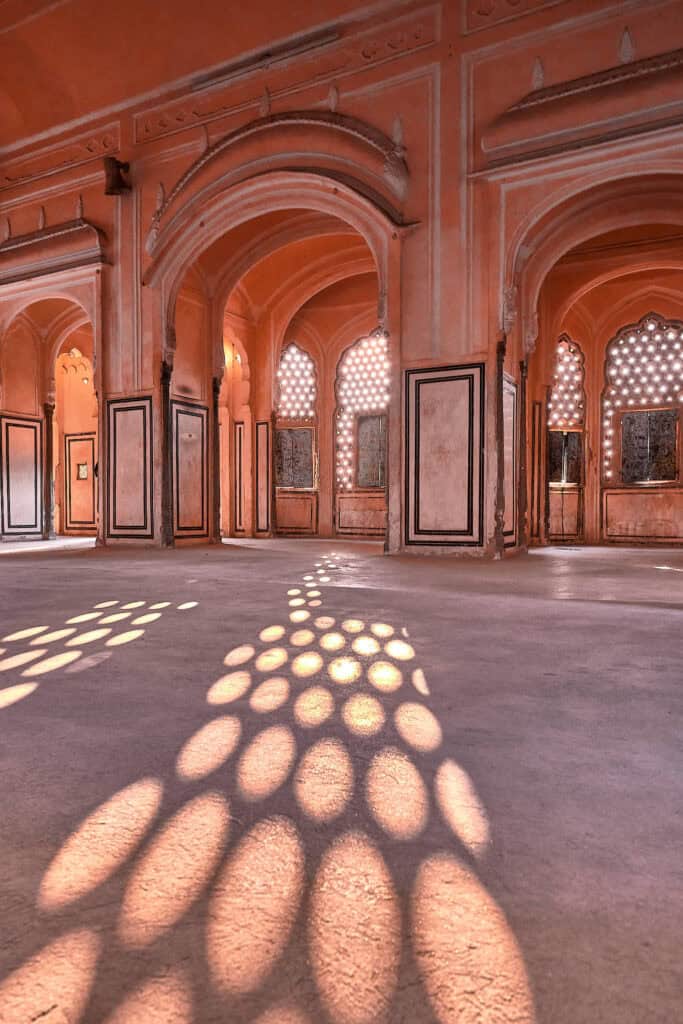 Interior of Hawa Mahal with sunlight streaming through ancient windows, creating a strong contrast of light and shadow across the walls